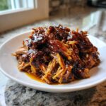 Close-up of tender, shredded Slow Cooker Honey Garlic Pulled Pork coated in a rich, glossy sauce on a white plate.