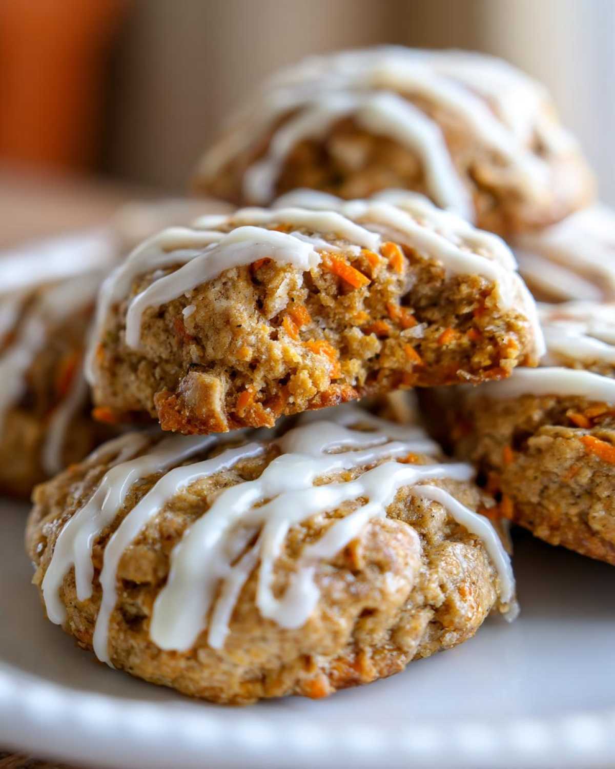 Close-up of Soft-Baked Carrot Cake Cookies drizzled with cream cheese glaze, one cookie is broken open.