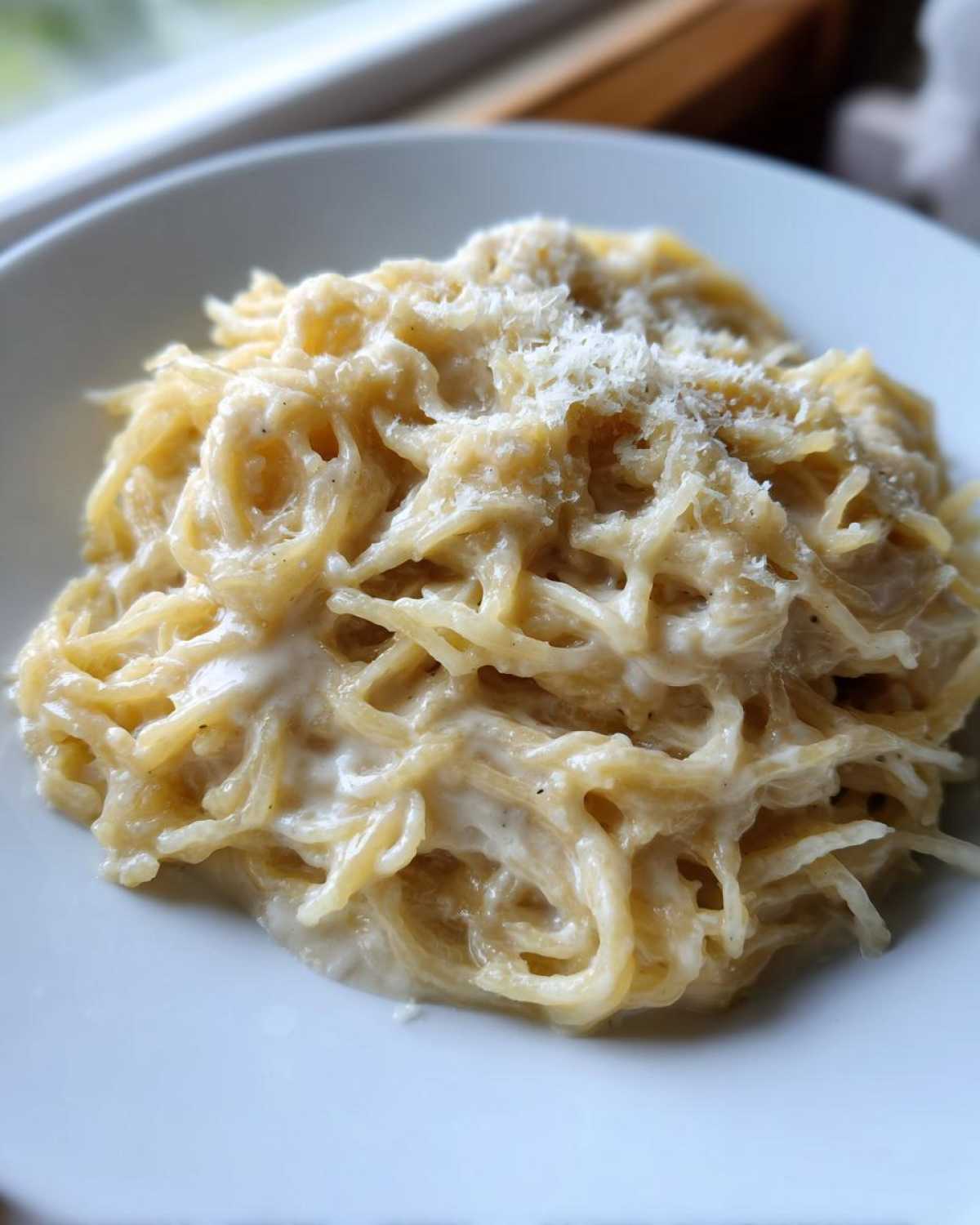 A close-up of a serving of Spaghetti Squash Alfredo tossed in a creamy white sauce and topped with grated cheese.