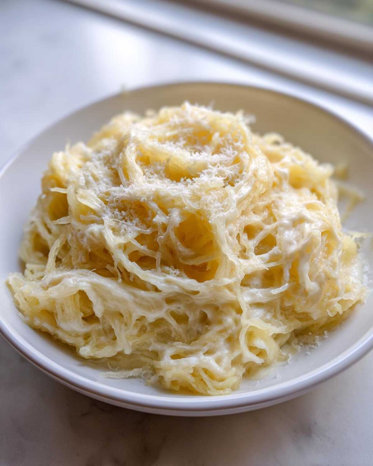 A close-up of creamy Spaghetti Squash Alfredo topped with grated Parmesan cheese served in a white bowl.
