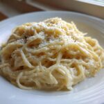 A close-up of creamy Spaghetti Squash Alfredo topped with grated Parmesan cheese and black pepper.