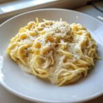 Close-up of a serving of Spaghetti Squash Alfredo tossed in a rich, creamy white sauce and topped with grated cheese and black pepper.