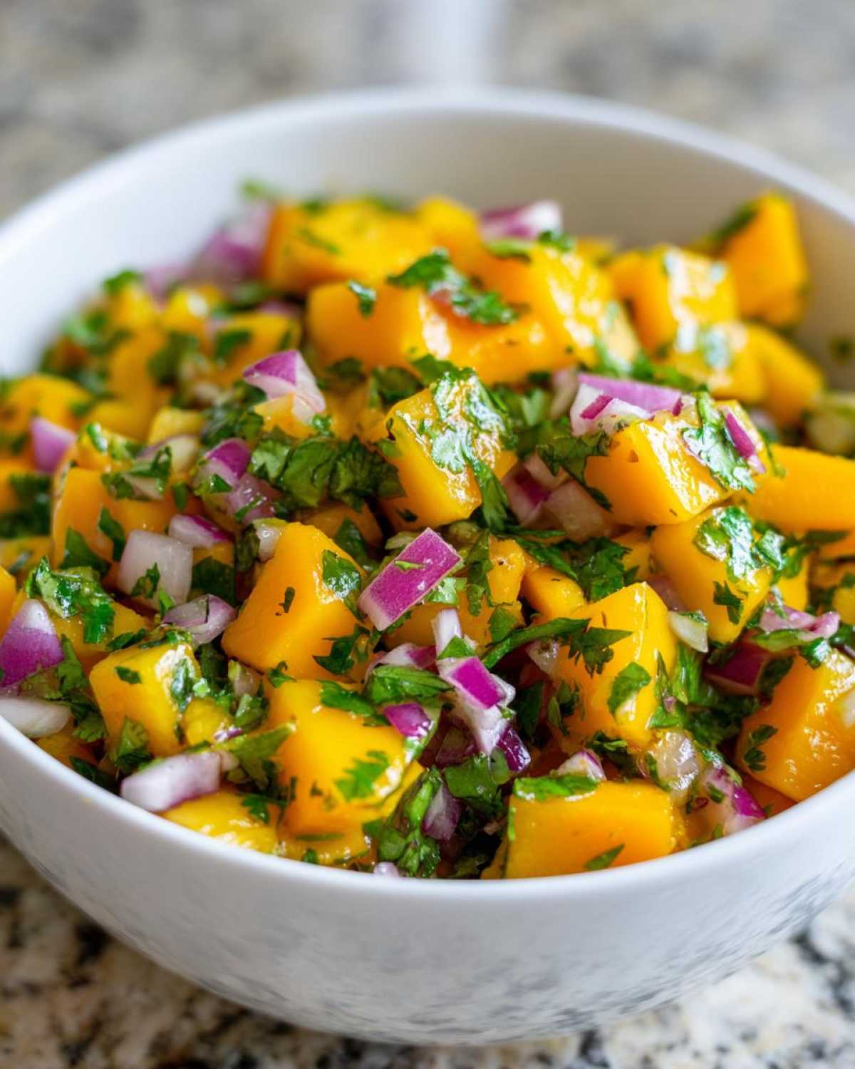 Close-up of vibrant Spicy Mango Salsa featuring diced mango, red onion, and cilantro in a white bowl.