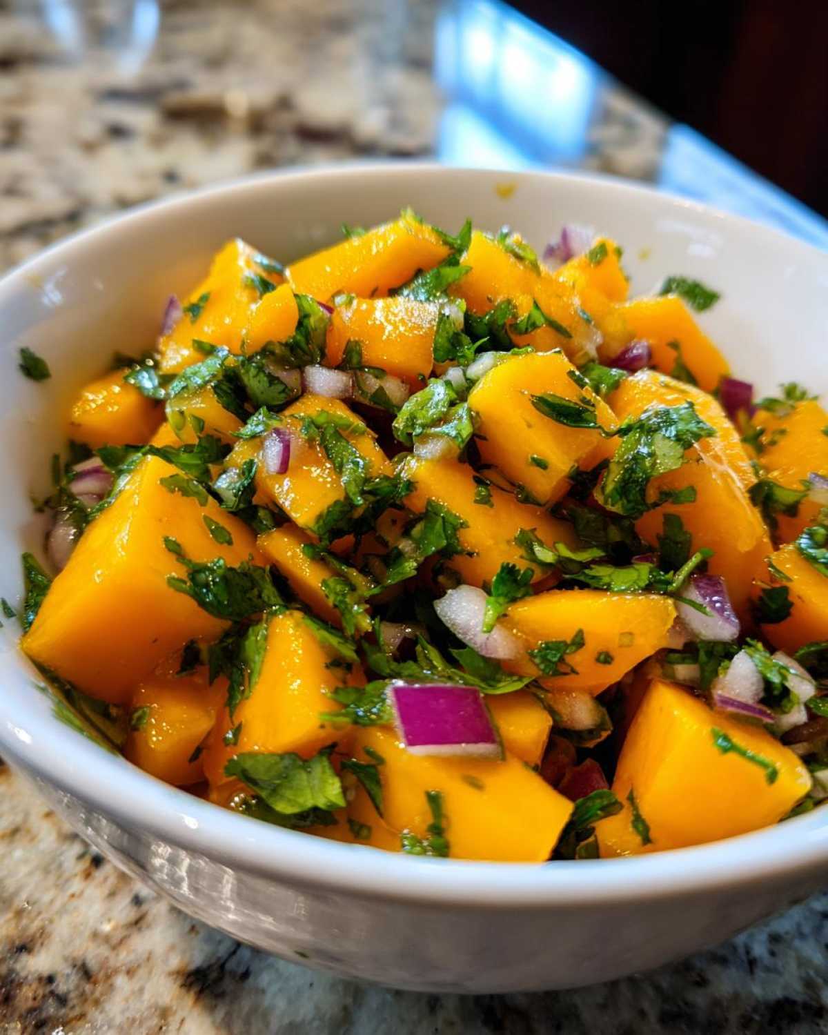Close-up of bright orange chunks of mango mixed with red onion and cilantro in a white bowl, ready for Spicy Mango Salsa.