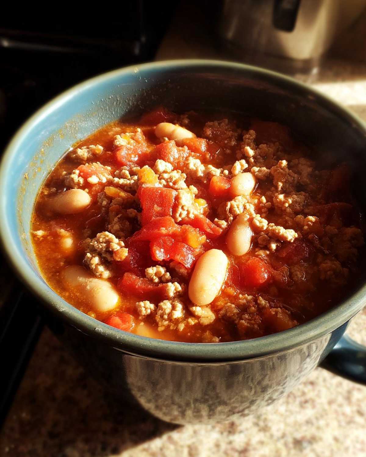 Close-up of steaming Spicy Turkey White Bean Chili featuring ground turkey, diced tomatoes, and white beans in a blue bowl.