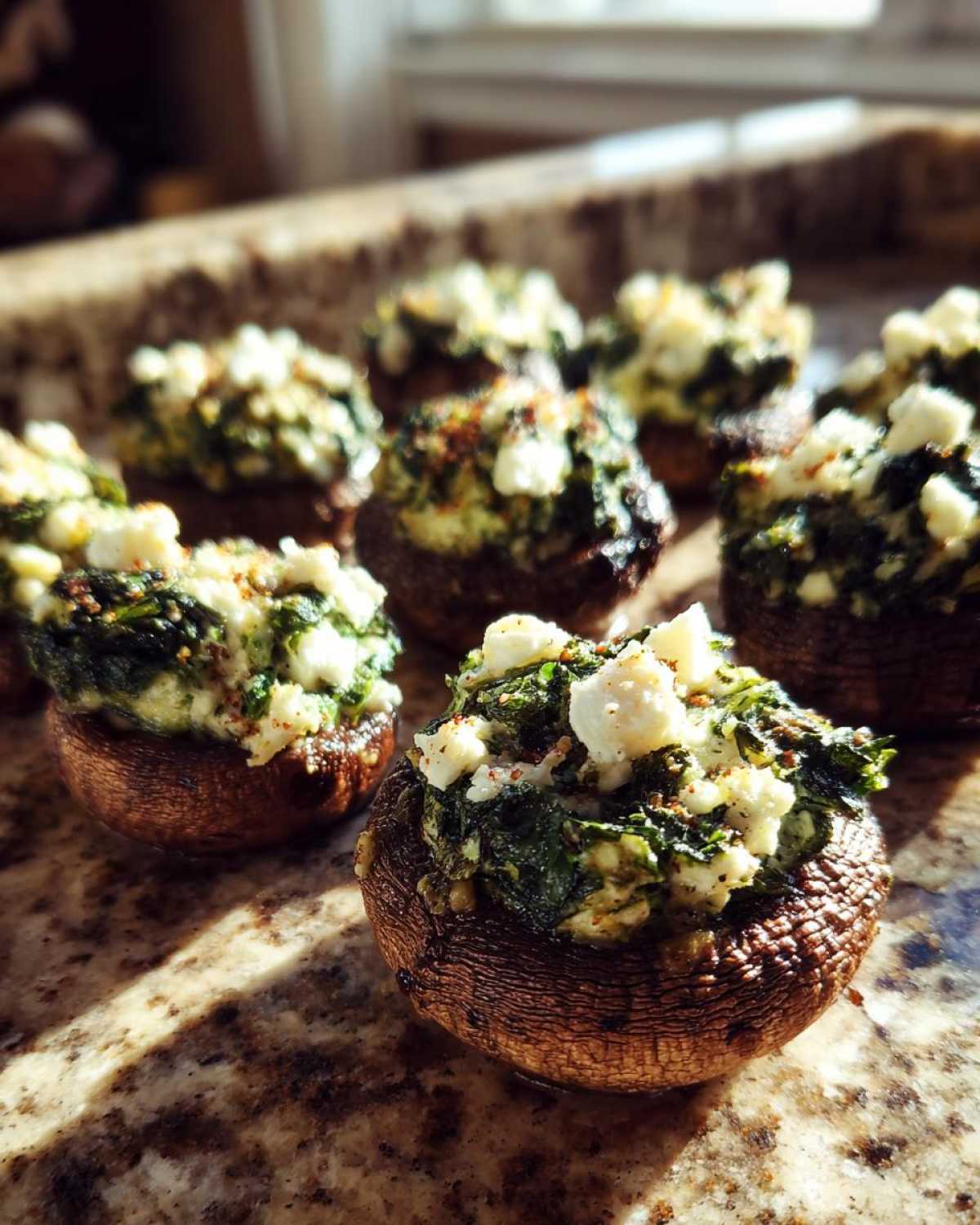 Close-up of baked Spinach and Feta Stuffed Mushrooms topped with crumbled feta cheese on a granite counter.