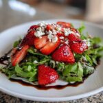 A vibrant Spring Mix Salad with Strawberries and Goat Cheese, drizzled with balsamic glaze on a white plate.