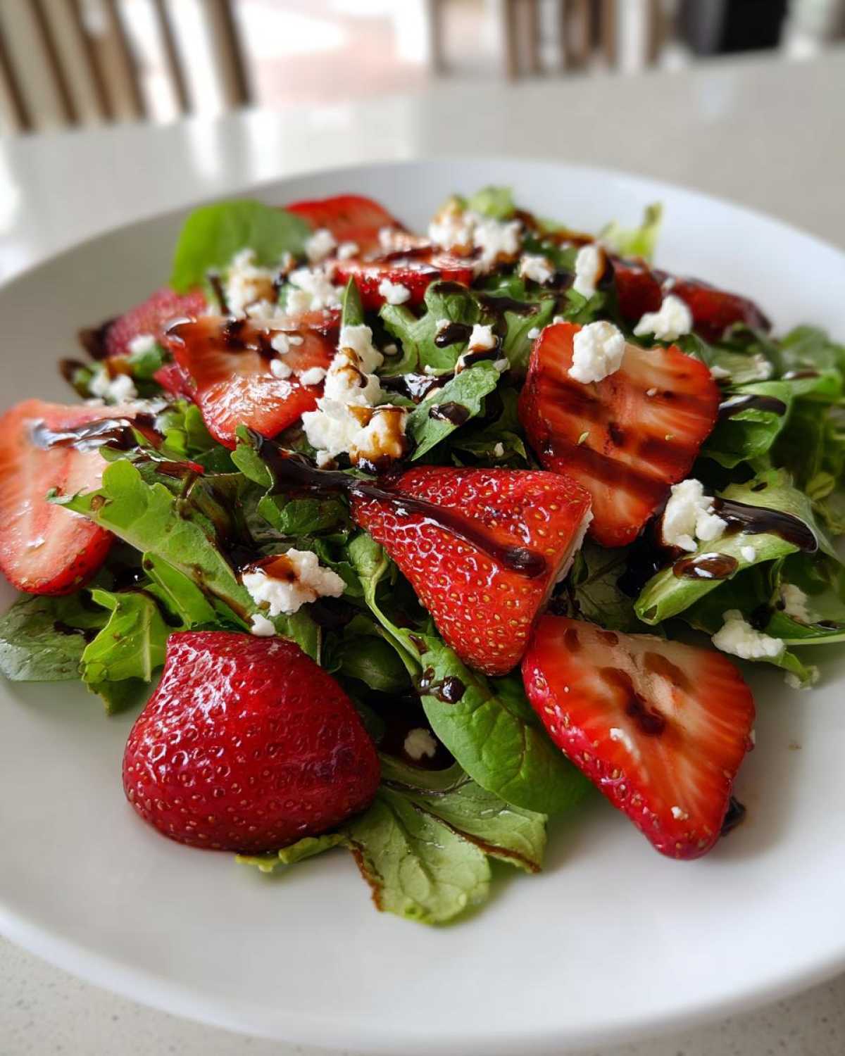 Close-up of a vibrant Spring Mix Salad with Strawberries and Goat Cheese drizzled with balsamic glaze.