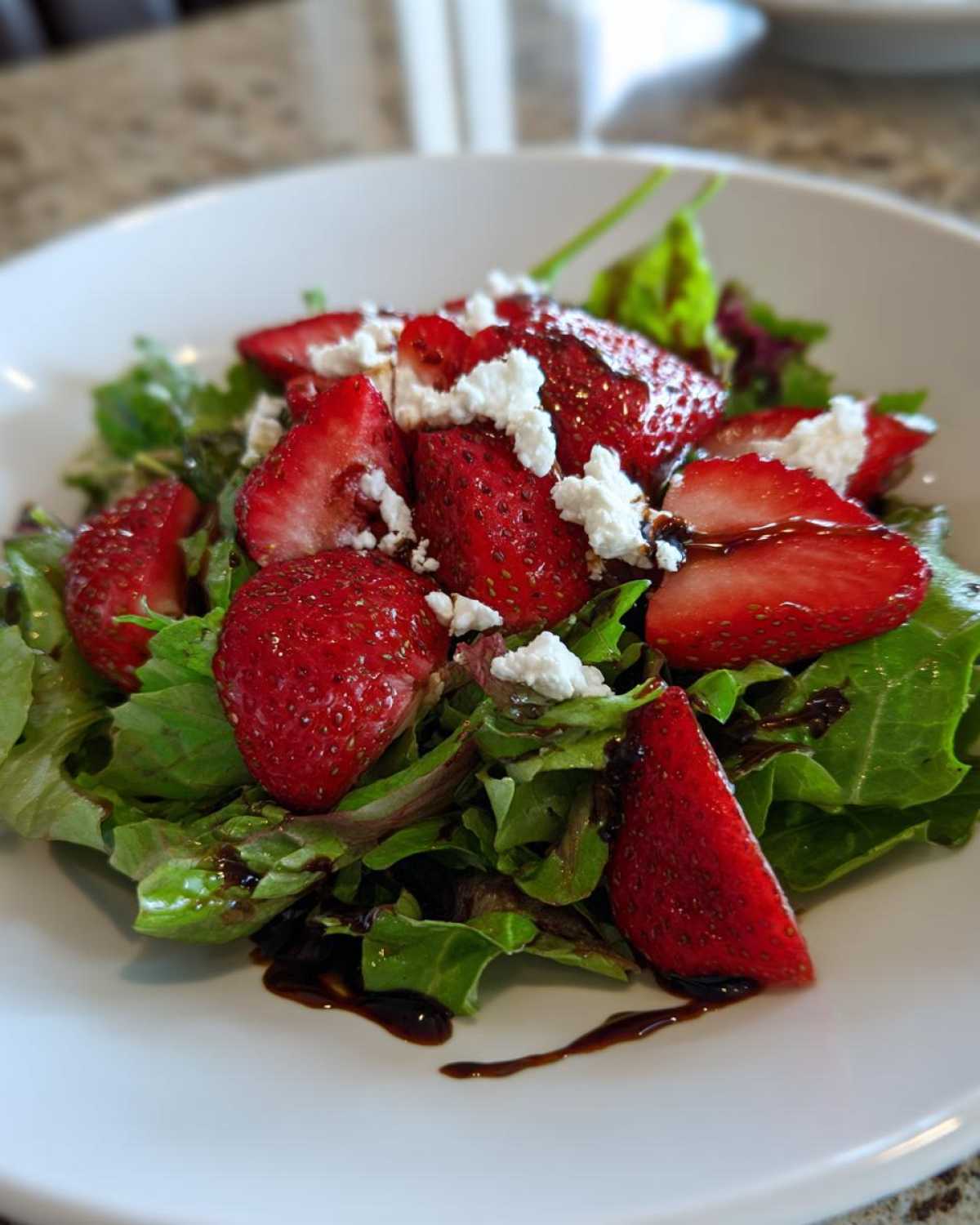 Close-up of a vibrant Spring Mix Salad with Strawberries and Goat Cheese topped with a balsamic glaze.