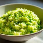 Close-up of vibrant green Spring Pea and Mint Risotto topped with fresh herbs in a light bowl.