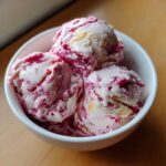 Three scoops of homemade Strawberry Banana Ice Cream swirled with bright pink fruit puree in a white bowl.