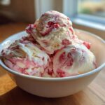 Several scoops of creamy Strawberry Banana Ice Cream with visible red fruit swirls in a white bowl.