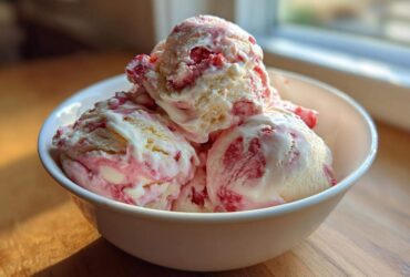 Several scoops of creamy Strawberry Banana Ice Cream with visible red fruit swirls in a white bowl.