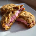 Close-up of a Strawberry Cheesecake Stuffed Cookie broken in half, showing creamy pink filling.