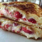 Close-up of two halves of golden brown Strawberry Cream Cheese Stuffed French Toast overflowing with filling.