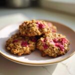 Three golden-brown Strawberry Oatmeal Breakfast Cookies stacked on a white plate, featuring visible oats and bright pink strawberry pieces.