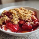 Close-up of a bowl of warm Strawberry Rhubarb Crisp topped with a buttery crumble and served over vanilla ice cream.