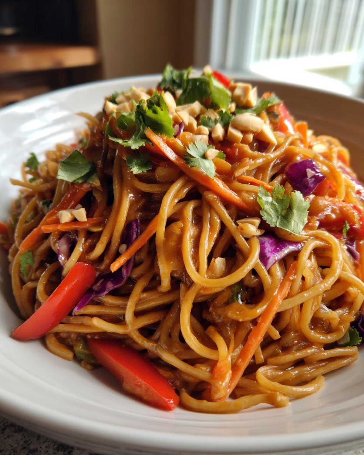 A close-up of a bowl filled with saucy Thai Peanut Noodles with Crunchy Veggies, topped with peanuts and cilantro.