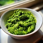 A close-up, brightly lit bowl filled with thick, vibrant green Vegan Basil Pesto.