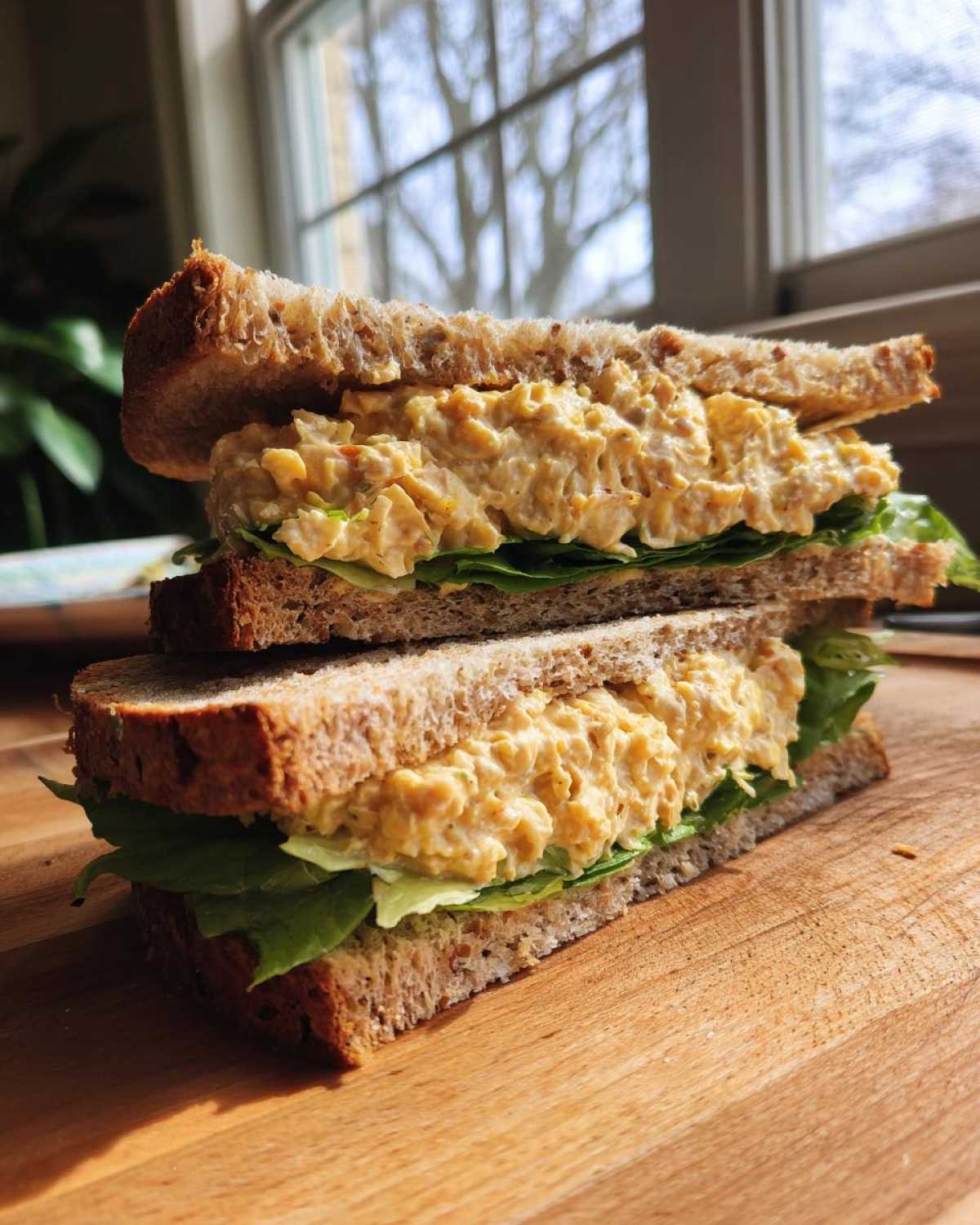 Two halves of a Vegan Chickpea Salad Sandwich stacked on a wooden board with lettuce.