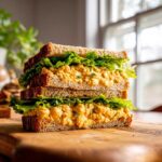 A tall, stacked Vegan Chickpea Salad Sandwich cut in half, showing creamy filling and crisp lettuce between whole wheat bread.
