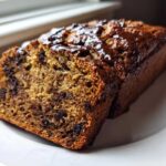 A close-up slice of moist Vegan Chocolate Banana Bread with melted chocolate drizzle on top, resting on a white plate.