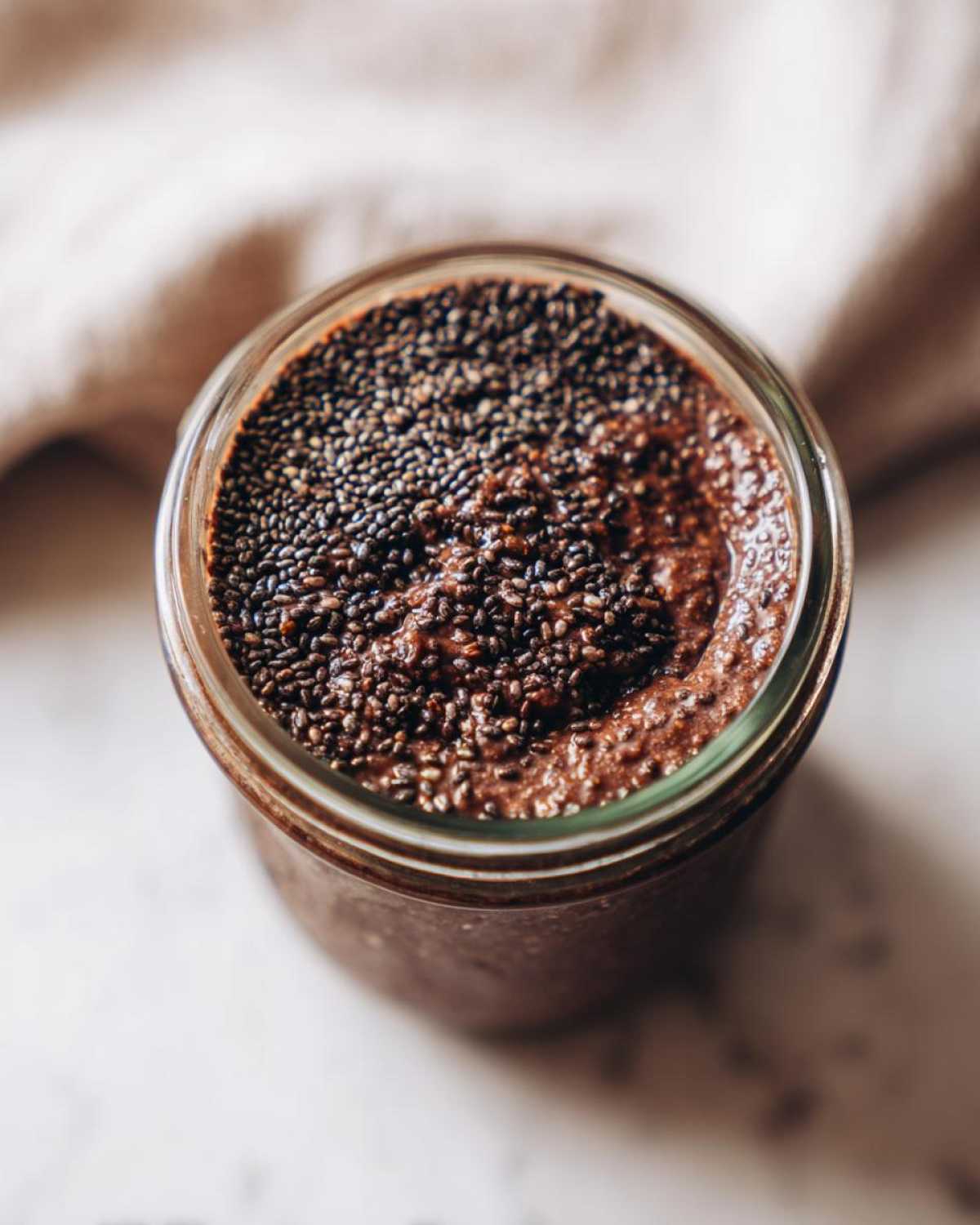 Overhead view of thick Vegan Chocolate Chia Pudding topped generously with dry chia seeds in a glass jar.