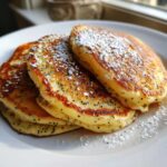 A stack of three fluffy Vegan Lemon Poppy Seed Pancakes dusted with powdered sugar.