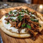 Close-up of Vegan Mushroom Shawarma served on a piece of pita bread with white sauce and fresh herbs.
