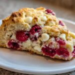 A close-up view of a freshly baked White Chocolate Raspberry Scones slice showing bright red raspberries and white chocolate chips.