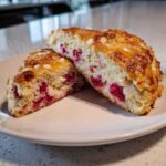 Two halves of freshly baked White Chocolate Raspberry Scones showing the moist interior with bright red raspberries and white chocolate chips.