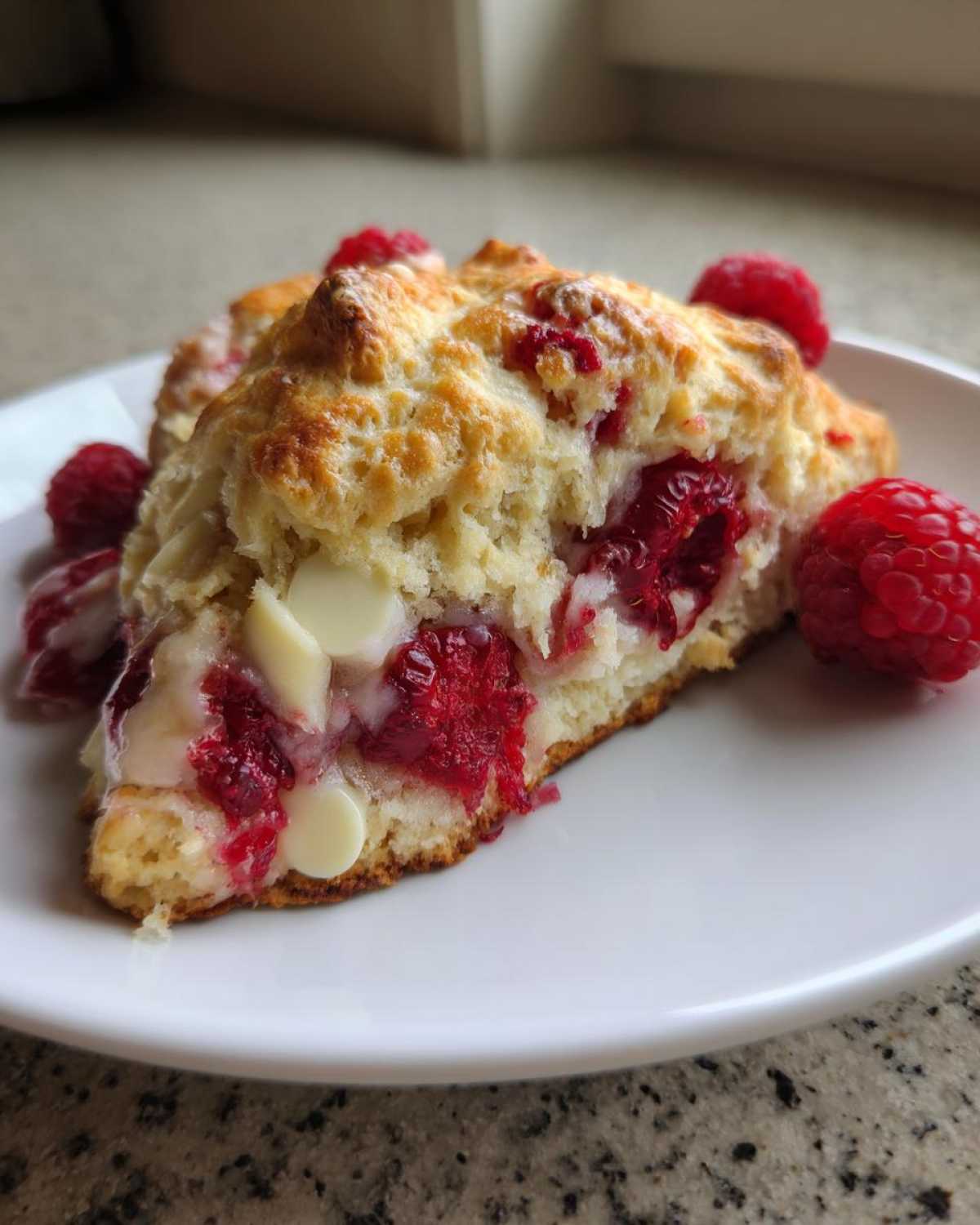 Close-up of a freshly baked White Chocolate Raspberry Scone, showing melted white chocolate chips and bright red raspberries inside.