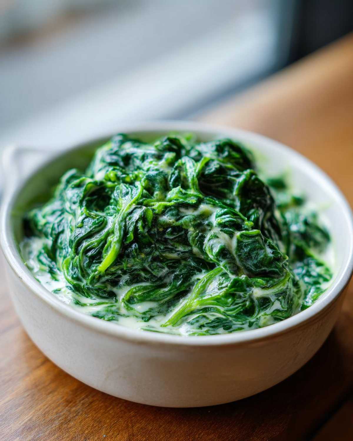 A close-up of vibrant green, perfectly cooked creamed spinach served in a small white bowl.