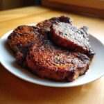 Three thick, beautifully seared 5-Spice air fryer pork chops resting on a white plate.