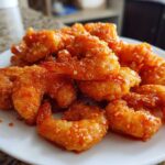 A pile of glistening, orange-glazed Air Fryer Crispy Buffalo Shrimp served on a white plate.