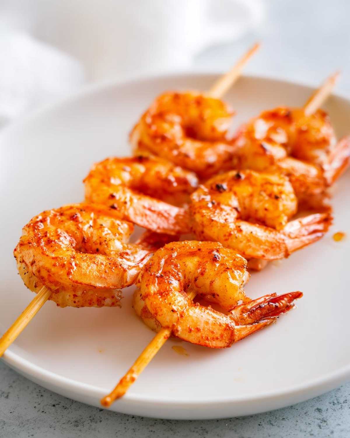 Close-up of several Air Fryer Crispy Cajun Shrimp Skewers seasoned with red spices, resting on a white plate.