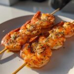 Close-up of three Air Fryer Crispy Cajun Shrimp Skewers seasoned with herbs on a white plate.