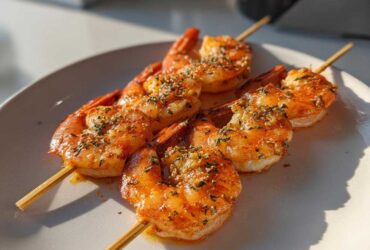 Close-up of three Air Fryer Crispy Cajun Shrimp Skewers seasoned with herbs on a white plate.