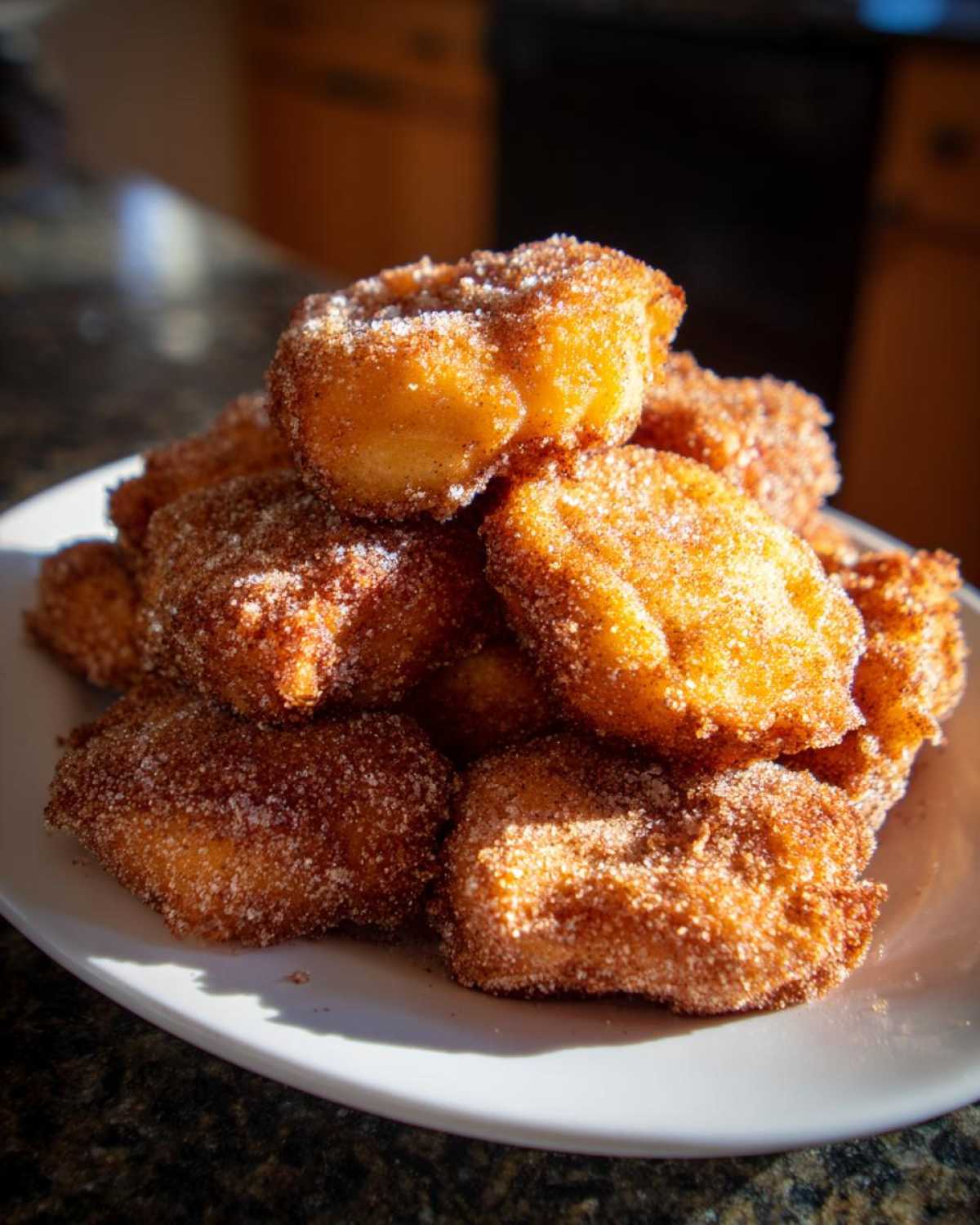 A close-up of golden brown Air Fryer Crispy Cinnamon Sugar Biscuit Bites piled high on a white plate.
