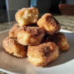 A stack of golden Air Fryer Crispy Cinnamon Sugar Biscuit Bites generously coated in cinnamon sugar on a white plate.