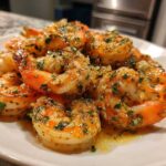 A close-up of perfectly cooked Air Fryer Crispy Garlic Butter Shrimp seasoned with herbs and butter sauce on a white plate.
