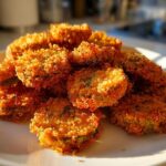 A pile of golden brown Air Fryer Crispy Garlic Dill Pickles slices on a white plate, highlighted by sunlight.