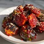 Close-up of crispy Air Fryer Crispy Gochujang Brussels Sprouts tossed in a spicy red glaze and sprinkled with sesame seeds.