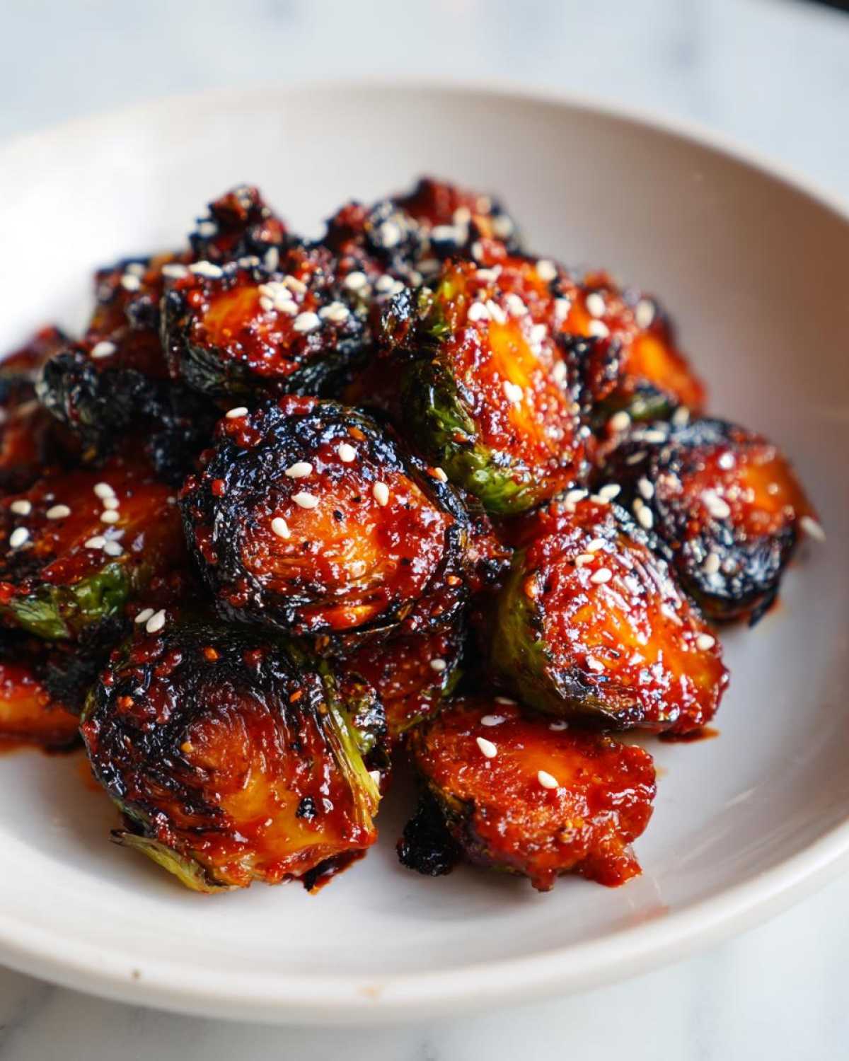 Close-up of crispy Air Fryer Crispy Gochujang Brussels Sprouts coated in a spicy glaze and sprinkled with sesame seeds.