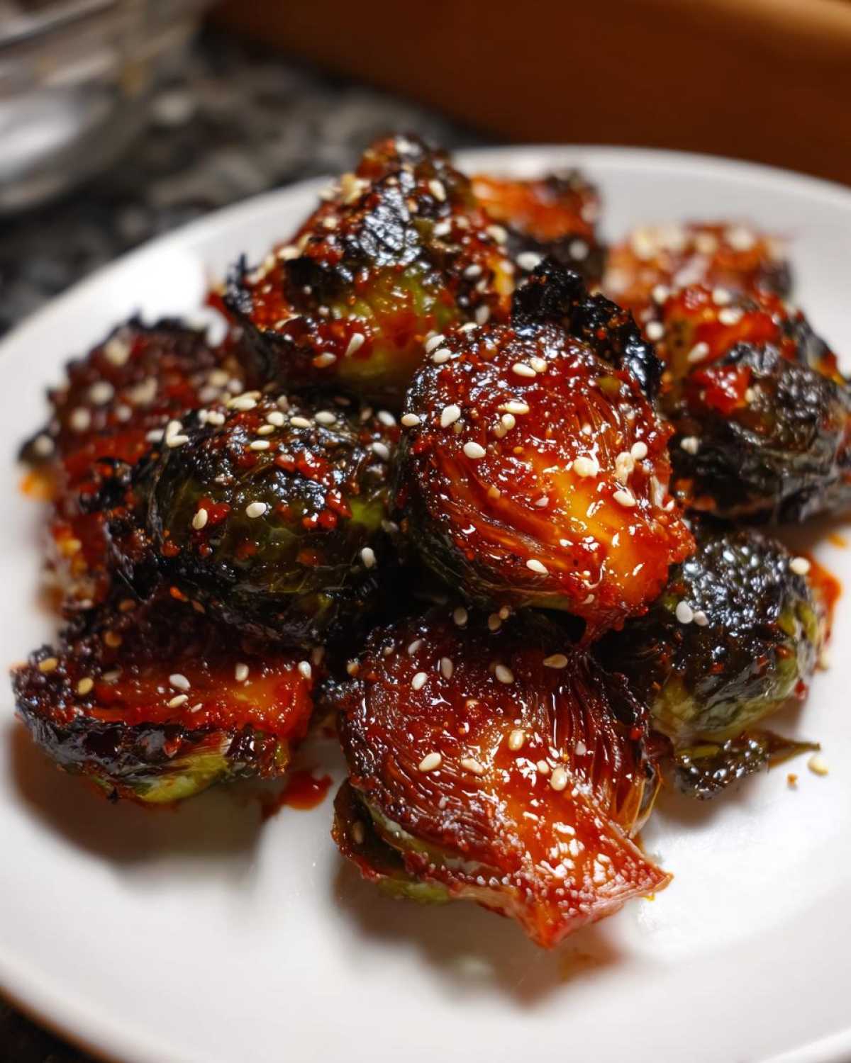 Close-up of crispy Air Fryer Crispy Gochujang Brussels Sprouts coated in a glossy red sauce and topped with sesame seeds.