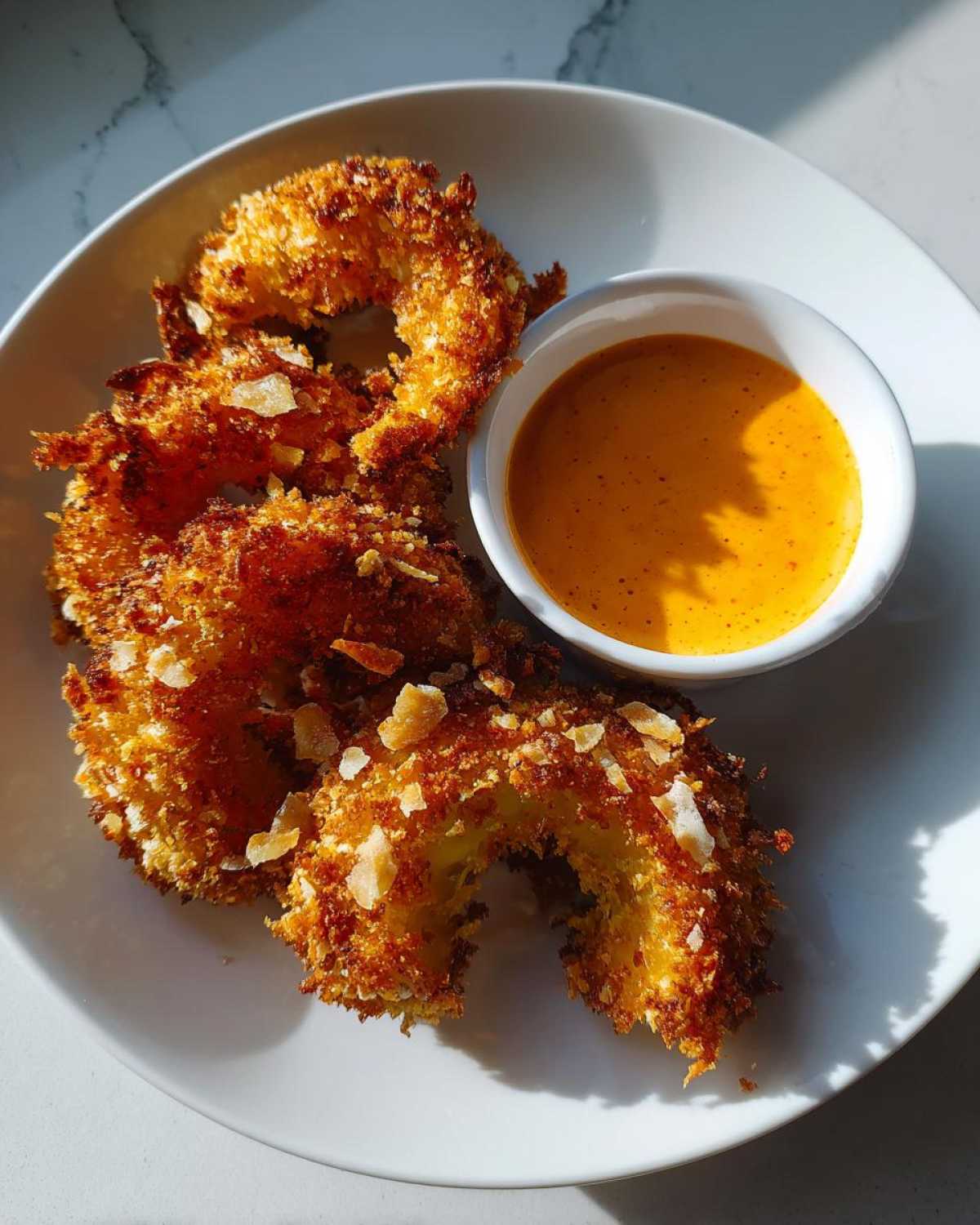 Golden brown Air Fryer Crispy Onion Petals served on a white plate next to a small bowl of orange spicy mayo.