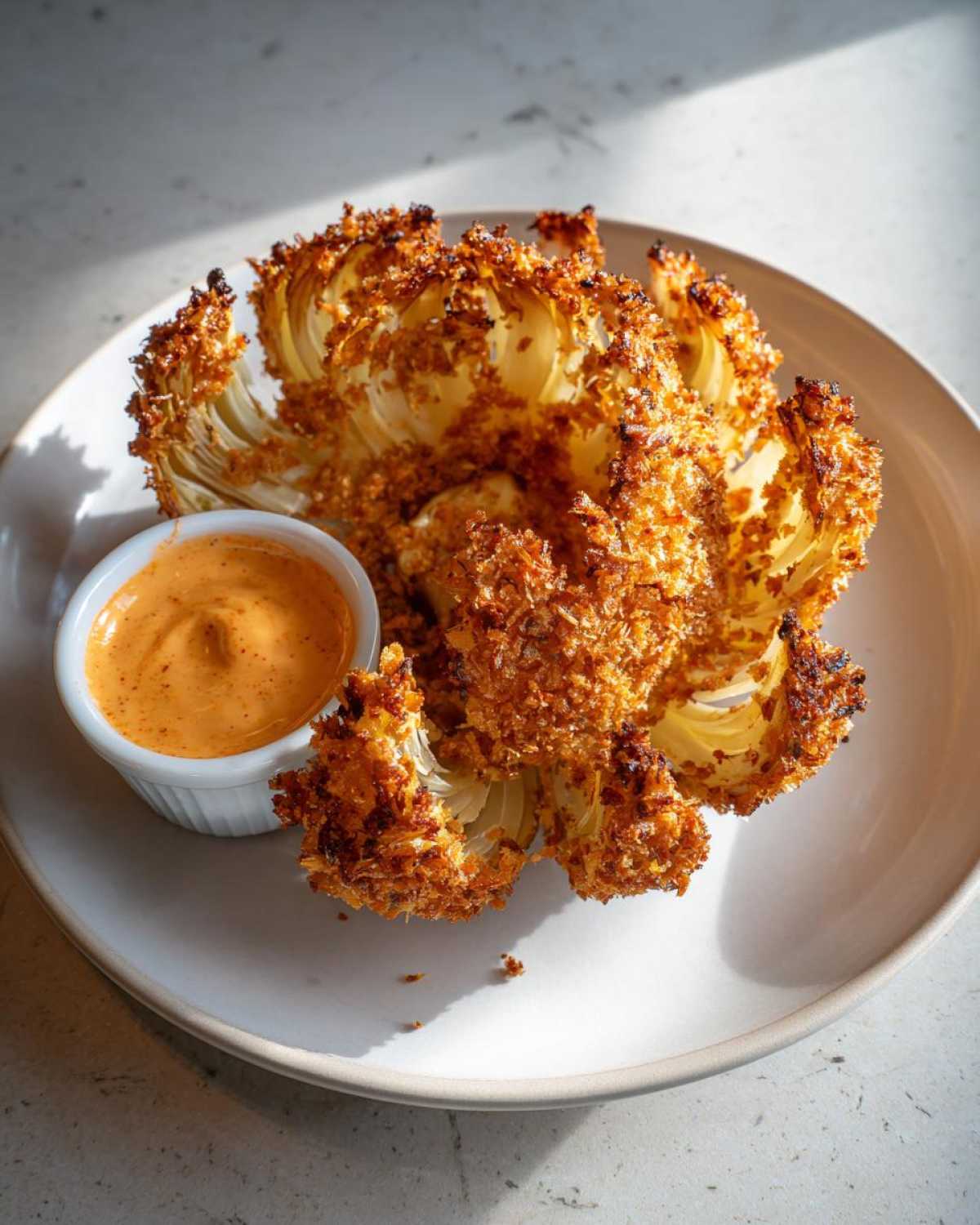 Golden brown, crispy air fryer onion petals served with a small ramekin of spicy mayo dipping sauce.