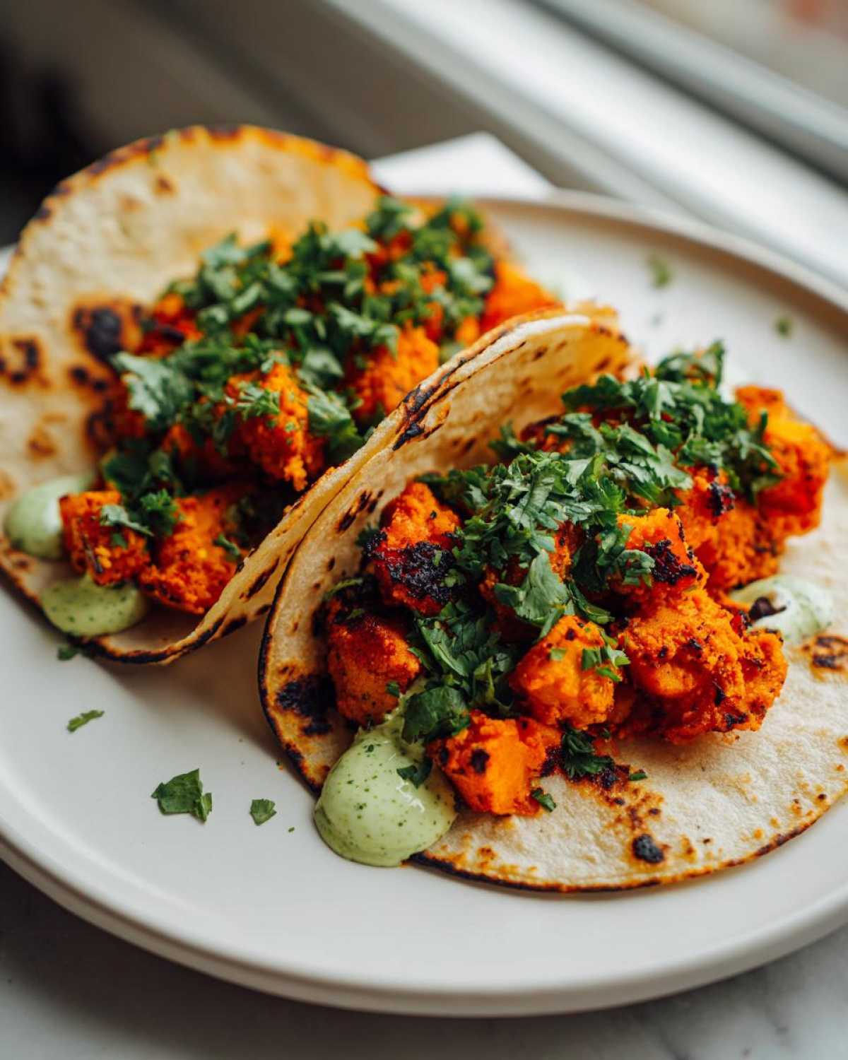 Two Air Fryer Crispy Sweet Potato Tacos filled with seasoned orange chunks, topped with fresh cilantro and green sauce.