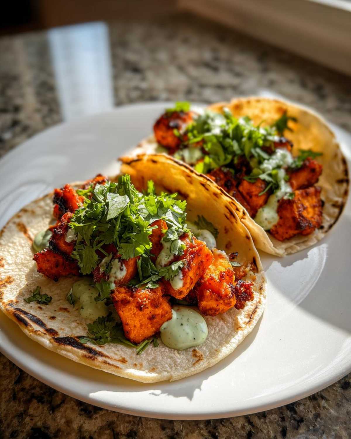 Two Air Fryer Crispy Sweet Potato Tacos topped with green sauce and fresh cilantro on a white plate.