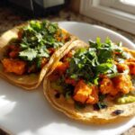Two warm tortillas filled with orange, seasoned sweet potato chunks and topped generously with fresh cilantro for Air Fryer Crispy Sweet Potato Tacos.